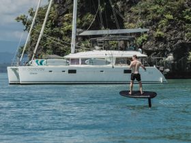 A thrilling moment captured as a man enjoys foiling in front of a beautiful catamaran, showcasing the excitement of water sports and adventure on the open sea.