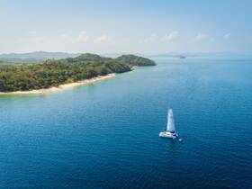 A stunning aerial view of a catamaran sailing through crystal-clear waters, surrounded by lush greenery and a serene coastline — perfect for exploring tropical destinations.
