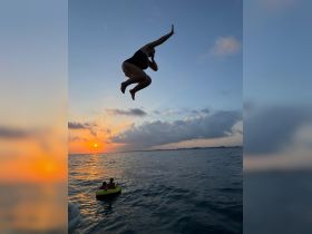A person leaps into the water at sunset, capturing the thrill of summer fun, while another child enjoys a ride on a float nearby.