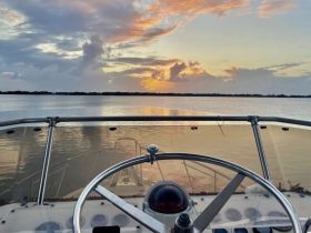 A serene view from the helm of a boat, overlooking a tranquil waterway at sunset — perfect for evening cruises and relaxation on the water.