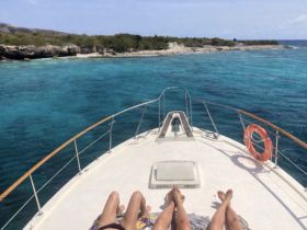Two individuals relax on the bow of a boat, enjoying the stunning turquoise waters and scenic coastline — a perfect getaway for sunbathing and relaxation.