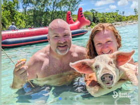 A couple enjoys a memorable experience swimming with a pig in crystal-clear waters, showcasing a unique wildlife encounter in the Bahamas.