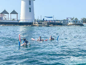 A group of snorkelers enjoys a fun day in the water near a picturesque lighthouse, showcasing the excitement of underwater exploration.