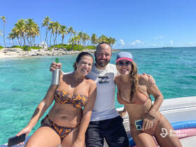 A joyful group of friends poses on a boat with clear turquoise waters and a tropical backdrop, perfect for a fun day out on the water.