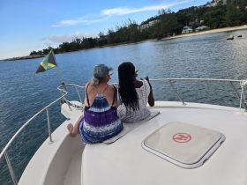 Two women enjoy a serene moment on the bow of a boat, overlooking calm waters and lush greenery — a perfect setting for relaxation and bonding.