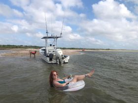 A woman relaxes on a float while enjoying a drink near a boat, with a playful dog nearby — a perfect day of leisure and fun on the water.