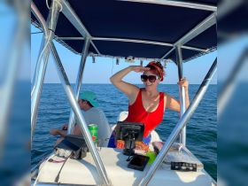 A woman in a red swimsuit salutes while enjoying a day on the water, with a companion in the background — capturing the essence of fun and adventure on a boat trip.