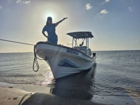 A woman poses joyfully beside a boat on the beach, with the sun creating a stunning backdrop — perfect for capturing memorable moments on the water.