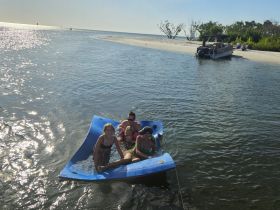 A fun group enjoys a sunny day on a floating mat in shallow waters, perfect for relaxation and family bonding during a sandbar stop.