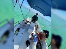 A couple enjoys a relaxing moment inside a boat, with the captain at the helm and beautiful turquoise waters visible outside — perfect for a day of adventure on the water.