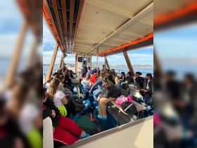 A group of students seated inside a boat, engaged in a presentation, showcasing the educational experience on the water.