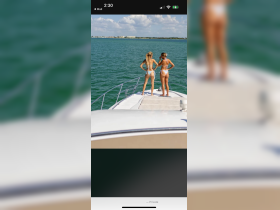 Two friends enjoy a sunny day on the bow of a boat, taking in the beautiful water views — perfect for a fun day out on the water.