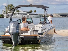 A couple enjoys a relaxing moment aboard a stylish boat, with a scenic backdrop of the shoreline and other vessels — perfect for a day of leisure on the water.