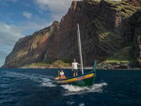 A scenic view of a small boat navigating through the ocean with dramatic cliffs in the background, showcasing the beauty of coastal adventures.