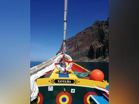 A vibrant view of the 'Xavelha' boat against a stunning rocky backdrop, showcasing its colorful design and sailing features.
