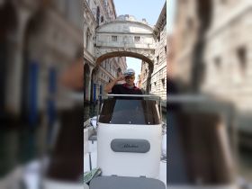 A boat captain poses with a salute in a picturesque Venetian canal, showcasing the charm of navigating through the historic waterways of Venice.