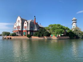 A picturesque view of a unique waterfront building surrounded by greenery, showcasing architectural beauty against a serene backdrop.