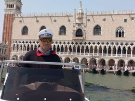A captain navigates a boat in front of the iconic Doge's Palace in Venice, showcasing the stunning architecture and vibrant atmosphere of this historic city.