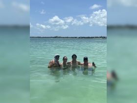 A cheerful group enjoys a refreshing swim in shallow waters, celebrating with drinks — a perfect moment for fun and relaxation at a sandbar.