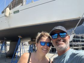 A couple poses for a selfie in front of their boat, showcasing the excitement of boat ownership and maintenance.