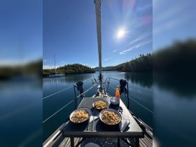 A beautifully set dining area on a sailboat featuring delicious meals against a serene water backdrop, perfect for enjoying gourmet experiences while sailing.
