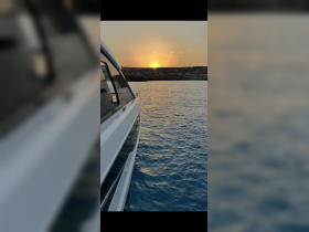 A stunning sunset view from the side of a yacht, showcasing the tranquil waters and the silhouette of the coastline — perfect for romantic evening cruises.