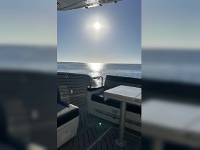 A serene view of the interior seating area on a boat, featuring a table and a stunning reflection of the sun on the water, perfect for relaxing outings.