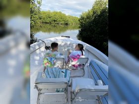 Two children enjoy a peaceful moment on a boat surrounded by lush mangroves, perfect for family adventures in nature.