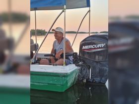 A man enjoys a serene moment at the helm of a small boat, showcasing the comfortable seating and tranquil waters around him.
