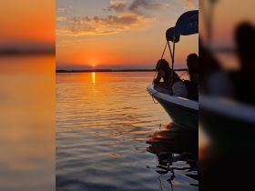 Two guests enjoy a serene sunset view from their boat, with vibrant colors reflecting on the water — a perfect moment for relaxation and appreciation of nature.