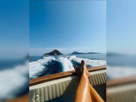 A serene view from a boat with a person's legs resting on the side, showcasing beautiful islands in the distance — perfect for a relaxing day on the water.