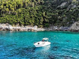 A scenic view of a boat anchored near a beautiful coastline, with a group of snorkelers enjoying the clear turquoise waters — an ideal setting for aquatic adventures.