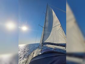 A stunning view of a sailboat under full sail, gliding across the shimmering ocean with the sun shining brightly overhead — perfect for showcasing sailing adventures.