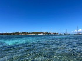 A stunning view of a serene coastline with multiple sailboats anchored in clear turquoise waters, perfect for a relaxing day on the water.