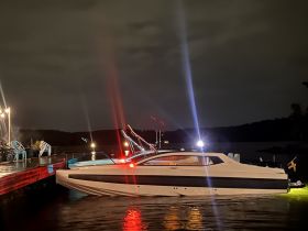 A sleek boat docked at night, illuminated by surrounding lights, creating a striking visual against the dark waters.