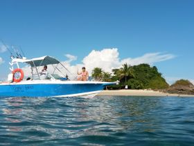 Guests wave from the boat 'Couba's Spirit' near a beautiful beach, capturing a fun day on the water in a tropical paradise.