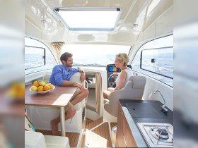 A cozy interior shot of a boat's helm area, featuring a couple engaged in conversation, with a bowl of fresh fruit on the table — perfect for enjoying time on the water.