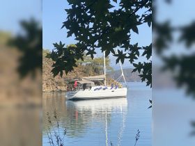 A serene view of a sailboat docked in calm waters, surrounded by lush greenery and mountains — perfect for a peaceful getaway.