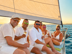 A cheerful group enjoys a sunset sailing experience, toasting with cocktails on the deck — perfect for celebrations and memorable moments on the water.