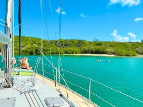 A serene moment on a sailboat with a guest relaxing while others enjoy the turquoise waters — a perfect snapshot of a tranquil sailing experience.