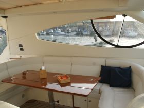 A cozy interior view of a boat's cabin featuring comfortable seating and a polished table, perfect for relaxing while enjoying the waterfront scenery.