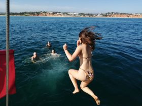 A lively scene of friends enjoying a day on the water, with one person jumping in while others swim nearby — perfect for summer adventures and beach fun.