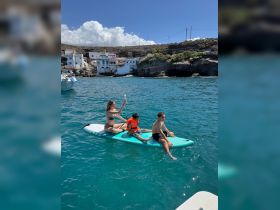 A family enjoys paddleboarding in clear waters, with kids having fun on the board — a perfect day for water activities and family bonding.
