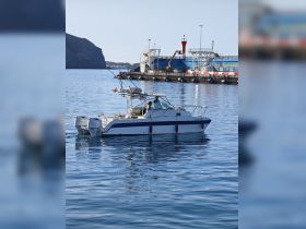 A sleek speedboat navigates the calm waters near a harbor, showcasing its design and the beautiful coastal backdrop.