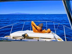 A person relaxes on the bow of a boat, enjoying the sun and ocean views — a perfect moment for fishing or leisure on the water.