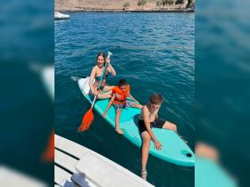 A fun family moment as a young girl paddles with two boys on a paddleboard in clear waters, showcasing the joy of water activities and family bonding.