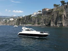 A sleek yacht navigates the waters near a stunning cliffside backdrop, showcasing the beauty of coastal cruising.