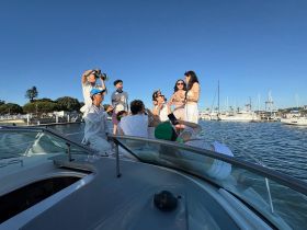 A lively group enjoys a boat party, celebrating with drinks and capturing memories against the backdrop of a marina. Perfect for social gatherings and special occasions on the water.