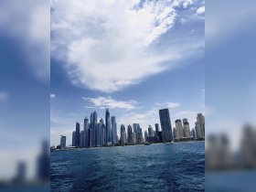 A stunning view of a modern skyline along the waterfront, showcasing the architectural beauty of the city against a bright blue sky — perfect for capturing the essence of urban adventures on the water.