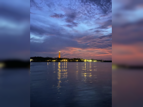 A stunning sunset view featuring a lighthouse and reflections on the water, creating a picturesque scene perfect for evening boat trips.